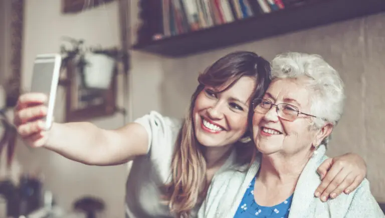 Eine junge Frau macht ein Selfie mit ihrer Oma im Wohnzimmer.
