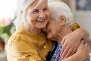 Zwei Frauen liegen sich lachend in den Armen, weil sie Entschädigung für Betreuung von Angehörigen erhalten