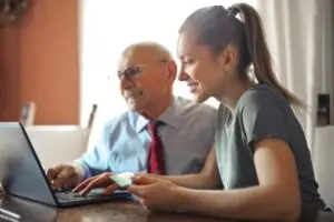 Pflege zu Hause: eine Frau mit ihrem Vater vor einem Laptop
