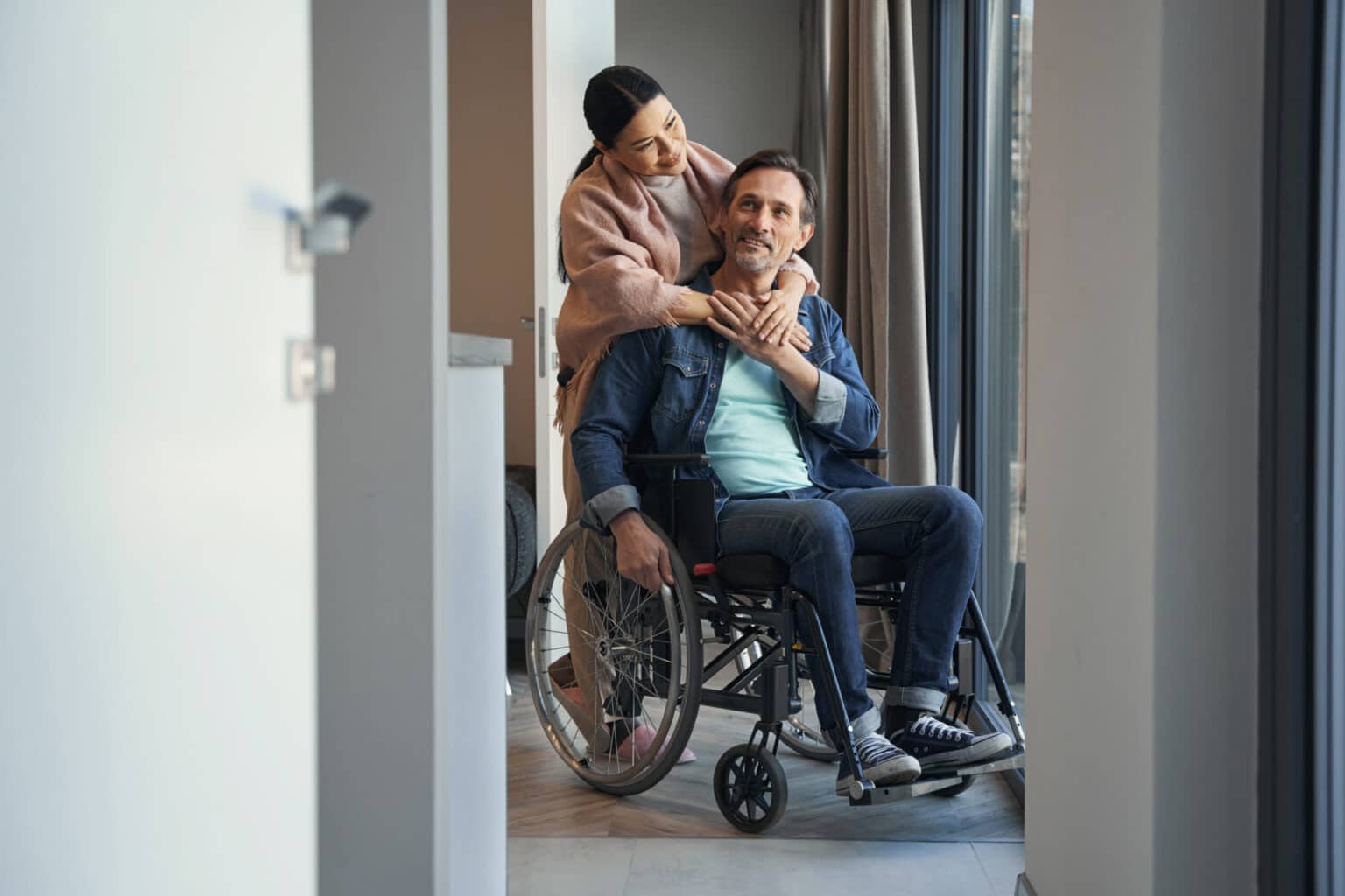 Pflegende Angehörige umarmt einen Mann, der im Rollstuhl sitzt.